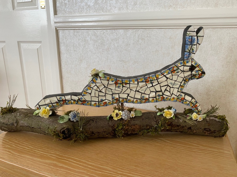 Running hare mosaic made from vintage china on log with vintage flower ornaments. Suitable for indoors or outdoors. Black grouting.